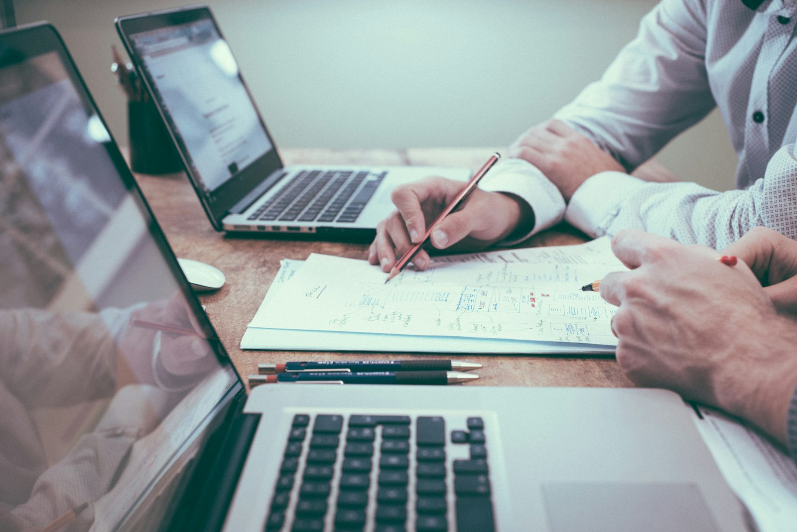 Person arbejder ved et skrivebord med notesbøger, laptop og planer lagt frem